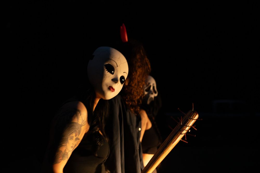 Two masked figures with torches pose menacingly in dramatic low-key lighting.