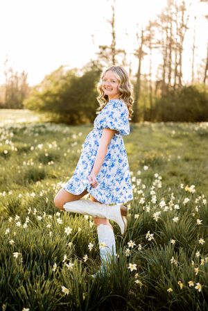 A flowing blue floral dress twirls in a spring meadow filled with daffodils at golden hour sunset.