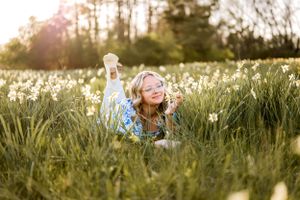 A teen lies joyfully in a meadow of white wildflowers during golden hour sunset.