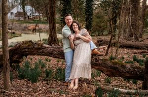 A couple embraces in a romantic forest setting with fallen logs and early spring foliage.