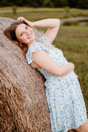 A series of outdoor portraits showing a person in a blue and white floral dress leaning against hay bales in warm sunlight.
