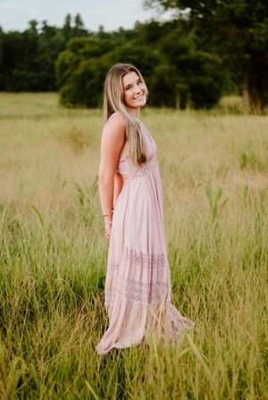 A person in a flowy pink dress poses gracefully in a sun-lit meadow during a summer photoshoot session.