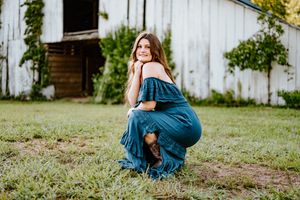 A figure in a flowing blue dress twirls playfully in a lush garden setting during a summer photoshoot.