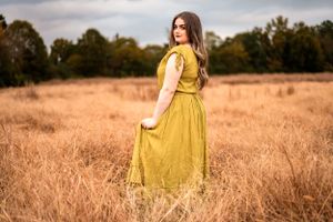 high school senior portrait in mustard yellow dress standing in golden autumn field.