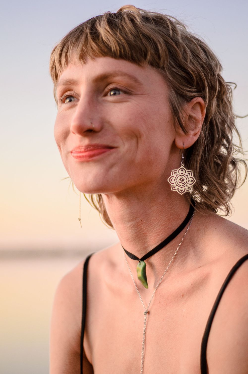 Close-up portrait showcasing ornate earrings and layered necklaces at sunset.