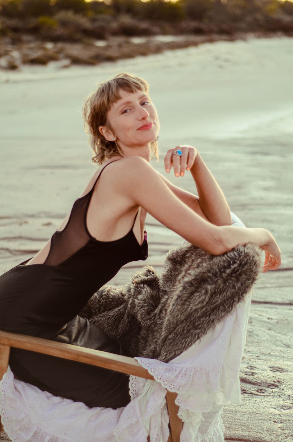 Beach portrait with black dress and fur accent against coastal backdrop.