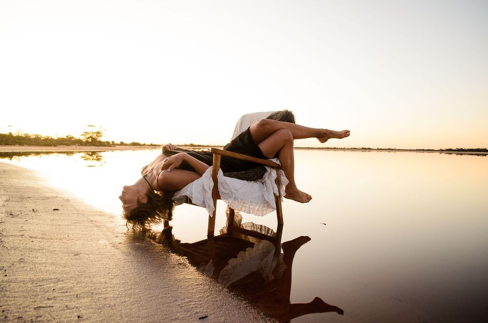 Dance performance on a reflective beach surface with golden sunlight creating dramatic shadows.