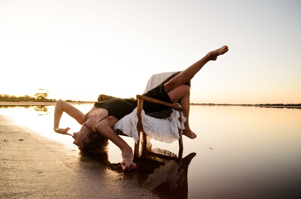 Contemporary dance pose performed on wet sand with mirror-like reflections at sunset.