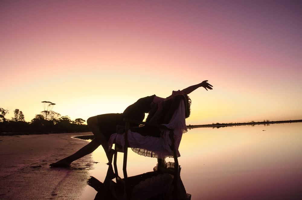 Dramatic silhouette of a dance performance on a beach during golden hour with perfect reflection.