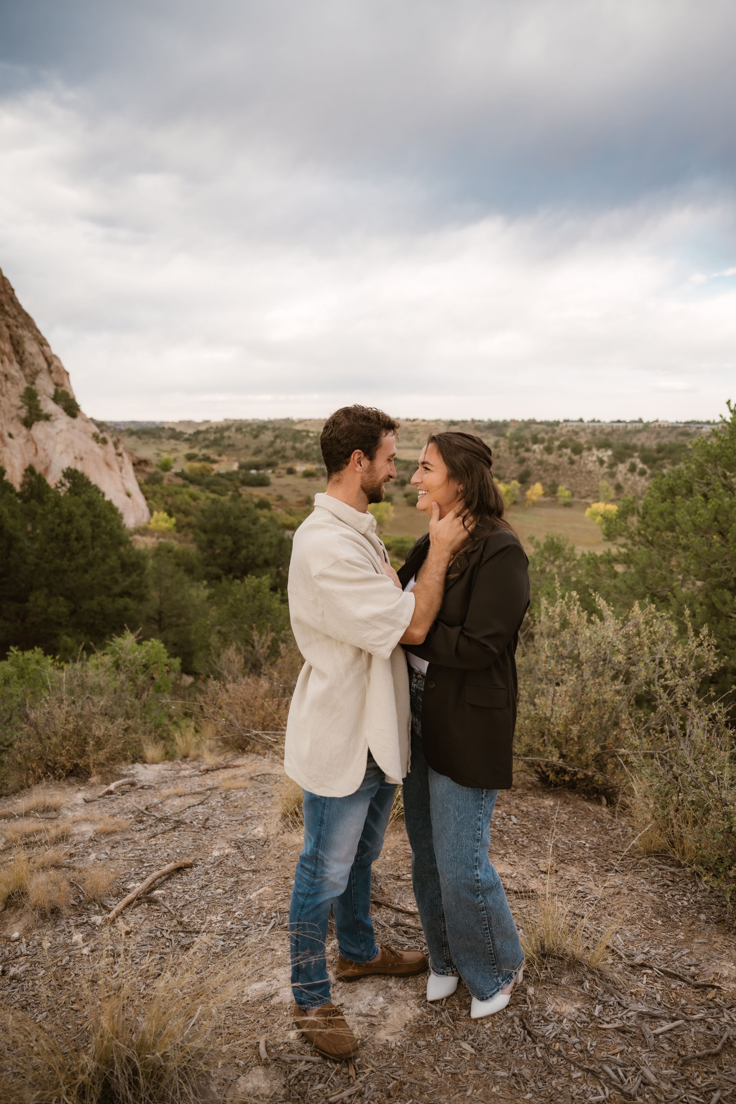 A couple embraces on rocky terrain with dramatic desert cliffs in the background.