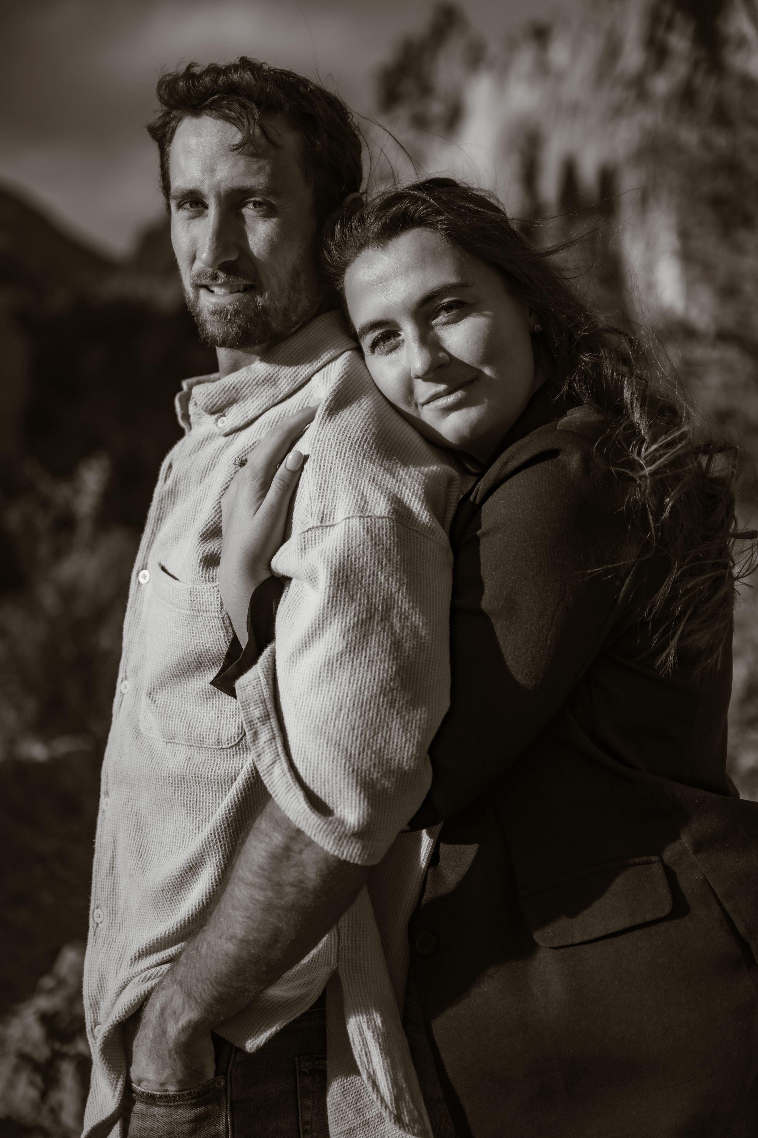 A couple in casual attire shares tender moments in black and white photography against natural scenery.