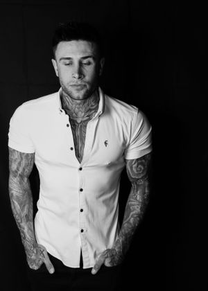 Portrait of tattooed man in white button-down shirt against dark background.