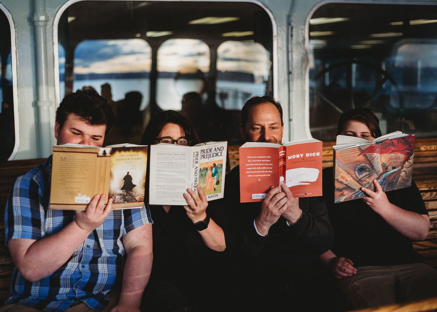 Group enjoying books while riding public transportation together on cushioned seats.