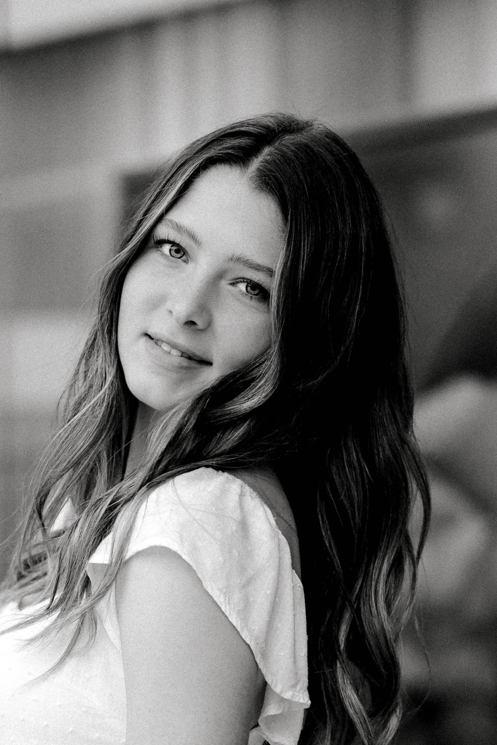 Black and white close-up portrait of a young brunette woman with long wavy hair smiling softly.