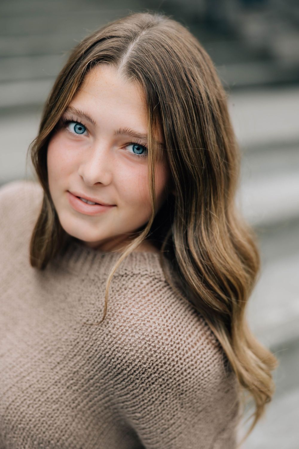 Close-up senior portrait of blue-eyed teen girl with long wavy hair wearing a beige knit sweater.