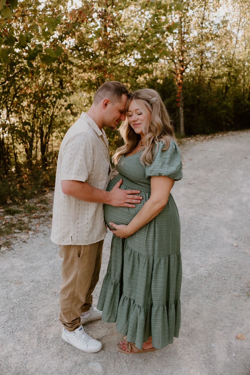 Expecting couple sharing intimate moment on gravel path during sunset maternity session.