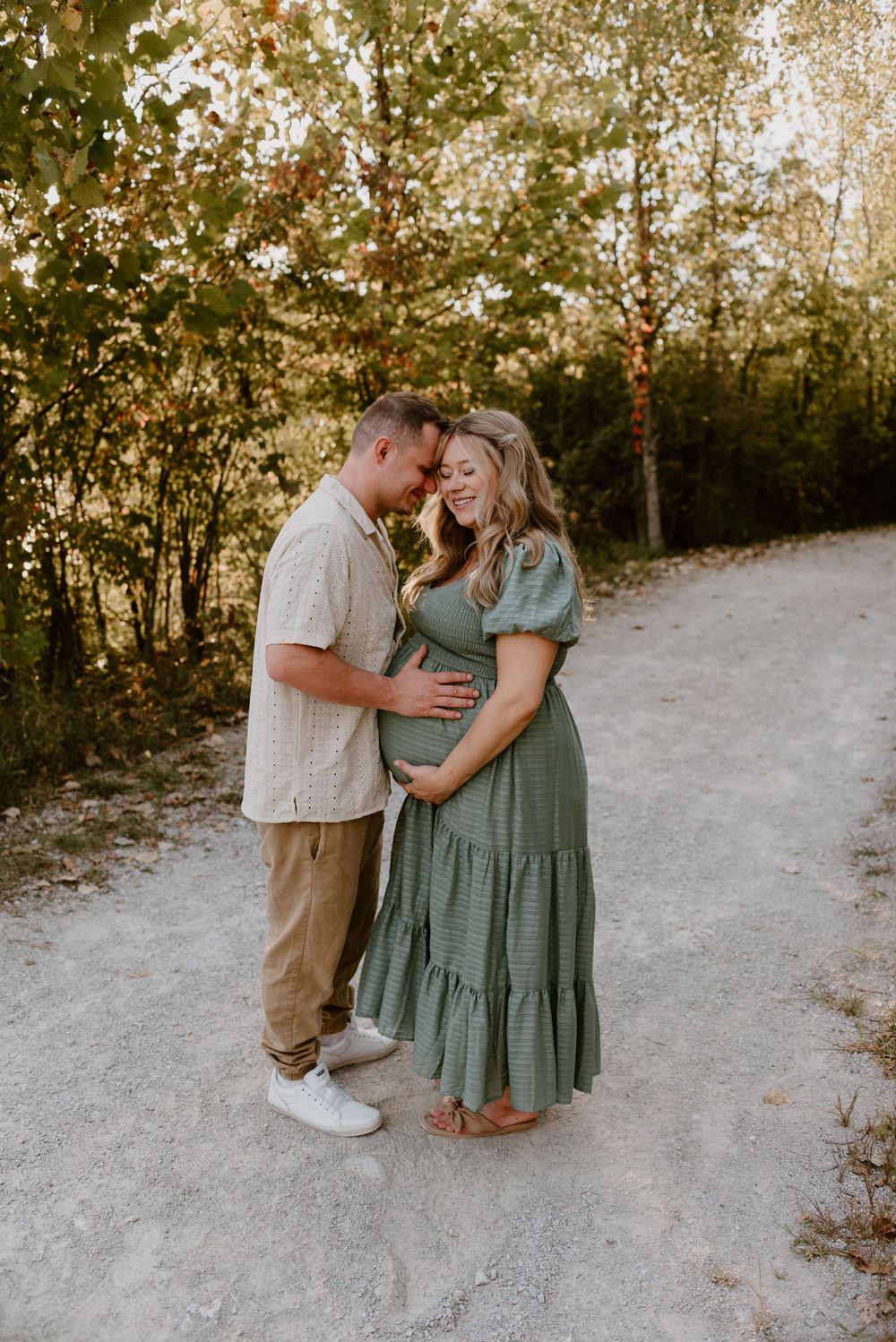 Intimate maternity photography session with couple in sage green dress outdoors.
