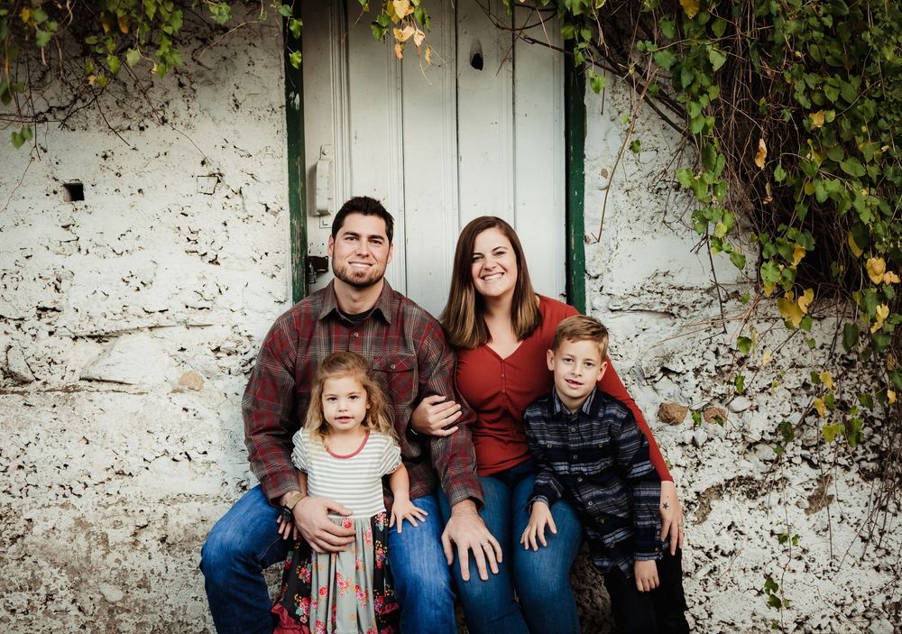 Family posing together against a rustic white wall with green vines.