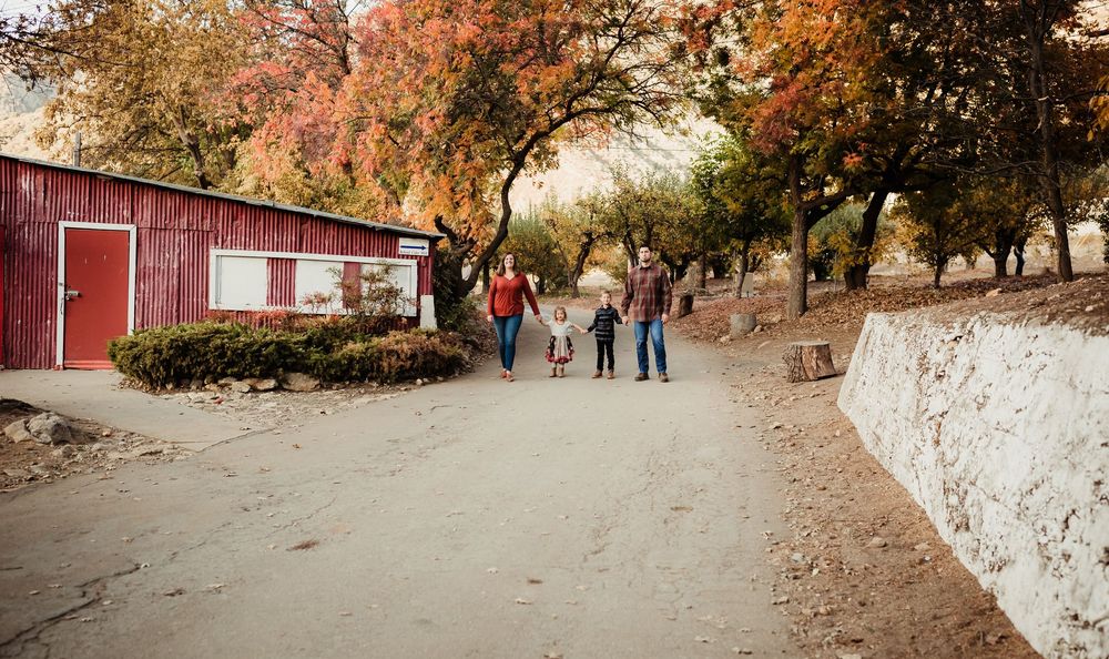A scenic autumn walkway with red barns and colorful fall foliage along a winding path in a park setting.
