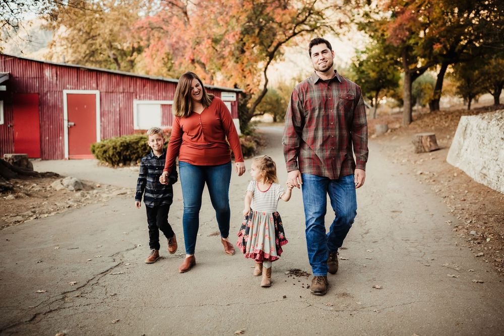 Family walking together on a path surrounded by fall foliage and a red barn.