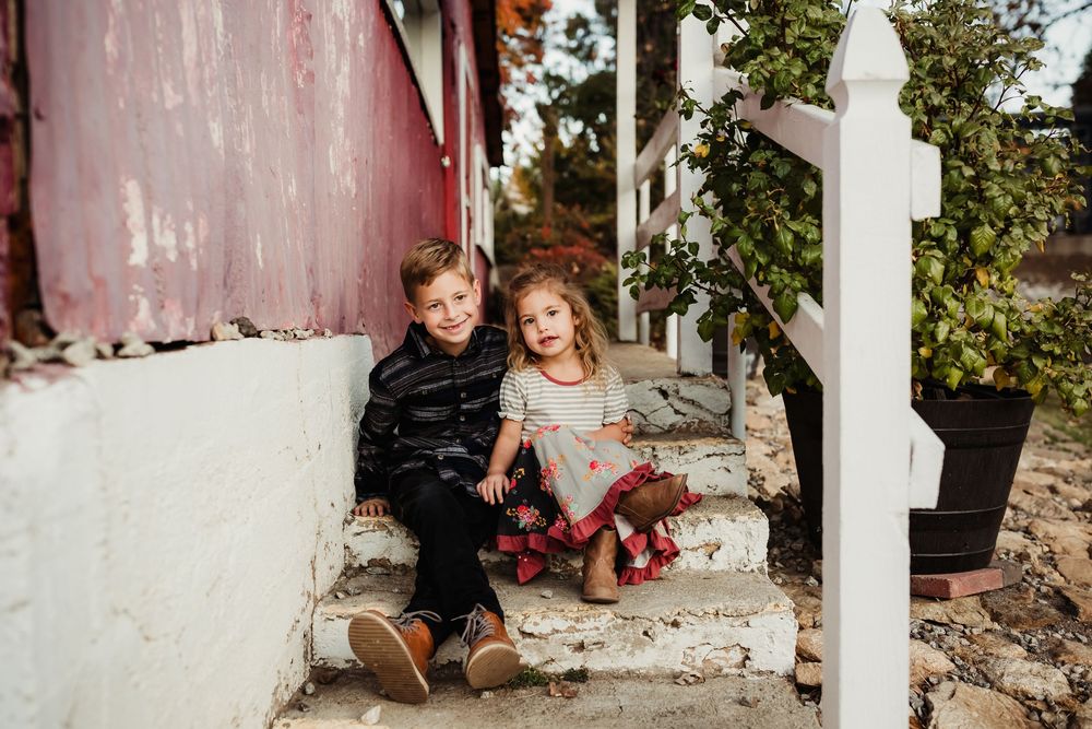 A couple sits together on white stone steps against a rustic wall during an autumn photo session.