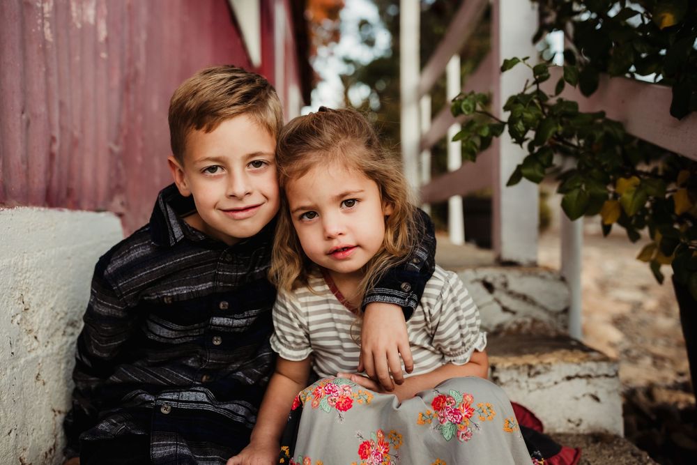 Children sitting together and smiling during an outdoor autumn family photo session.