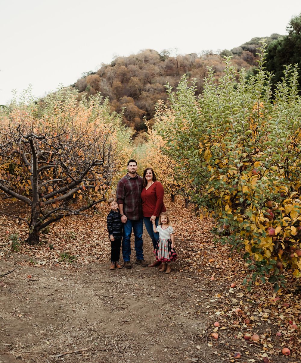 A group stands in an autumn orchard with golden leaves and bare branches creating a seasonal outdoor scene.