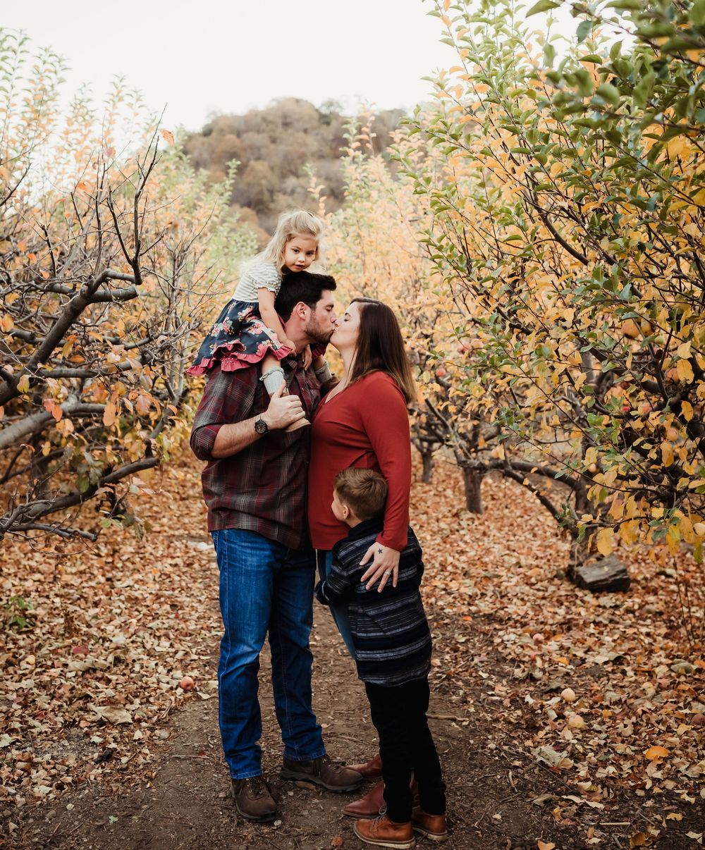 A family shares intimate moments among fall foliage in an orchard setting during golden hour.