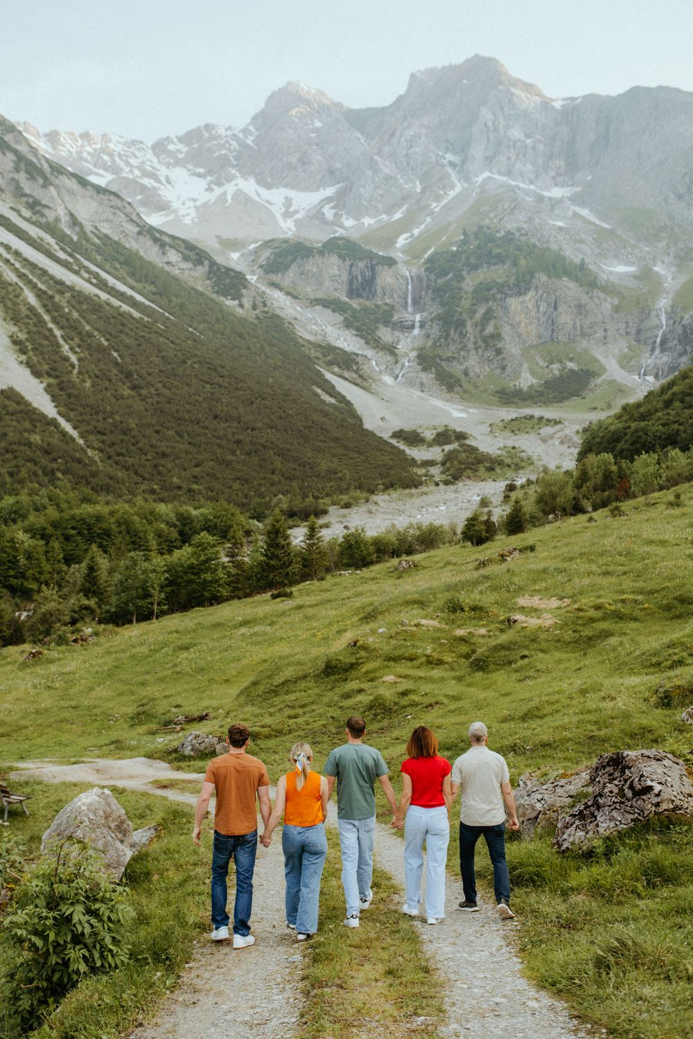 Group walking together on a mountain trail with scenic alpine peaks and green slopes in the background.