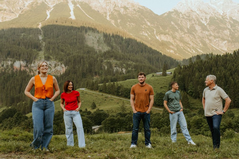 Group walking along a scenic mountain trail with distant peaks and green meadows.