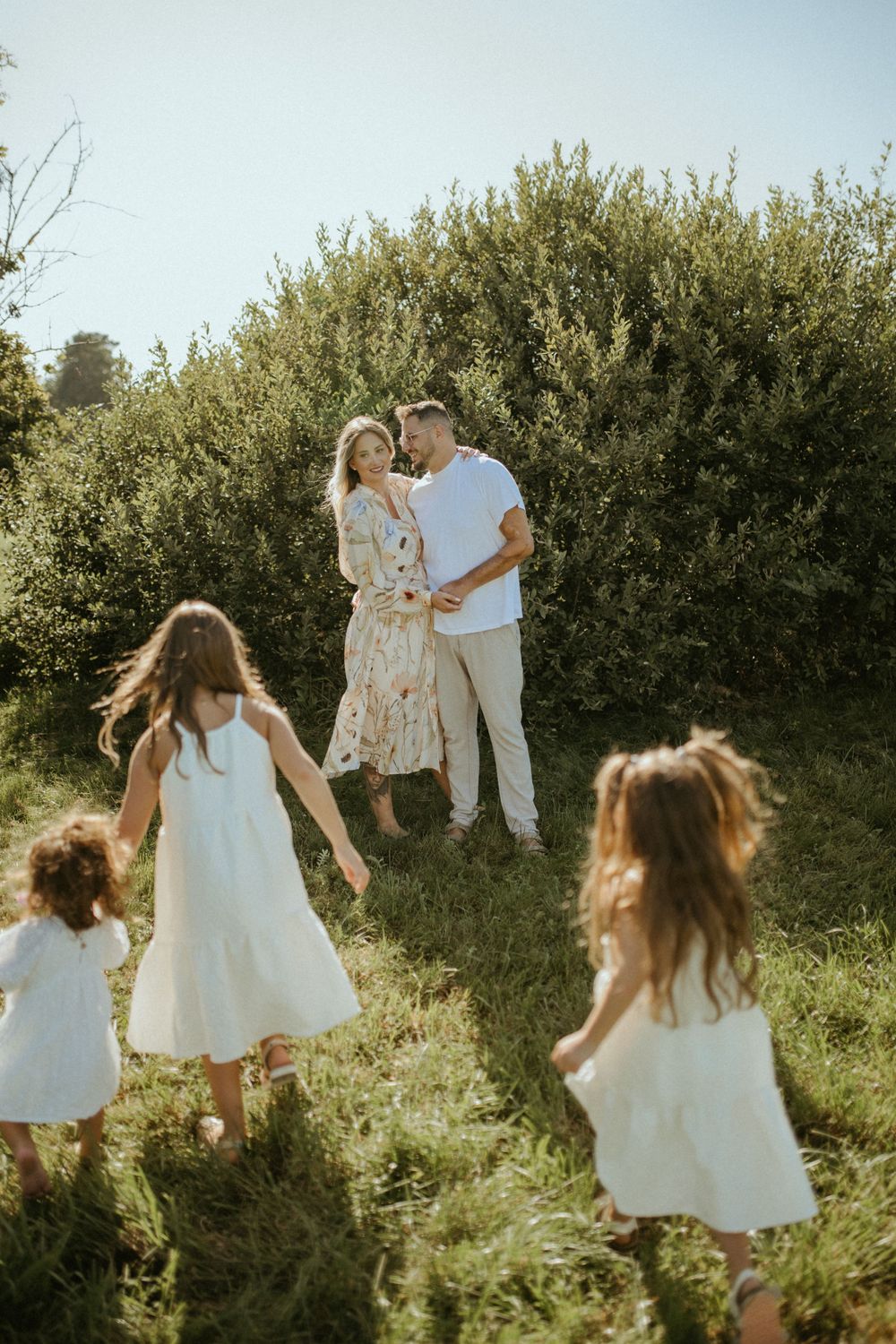 Family playing together in a sunlit meadow with green bushes in the background.