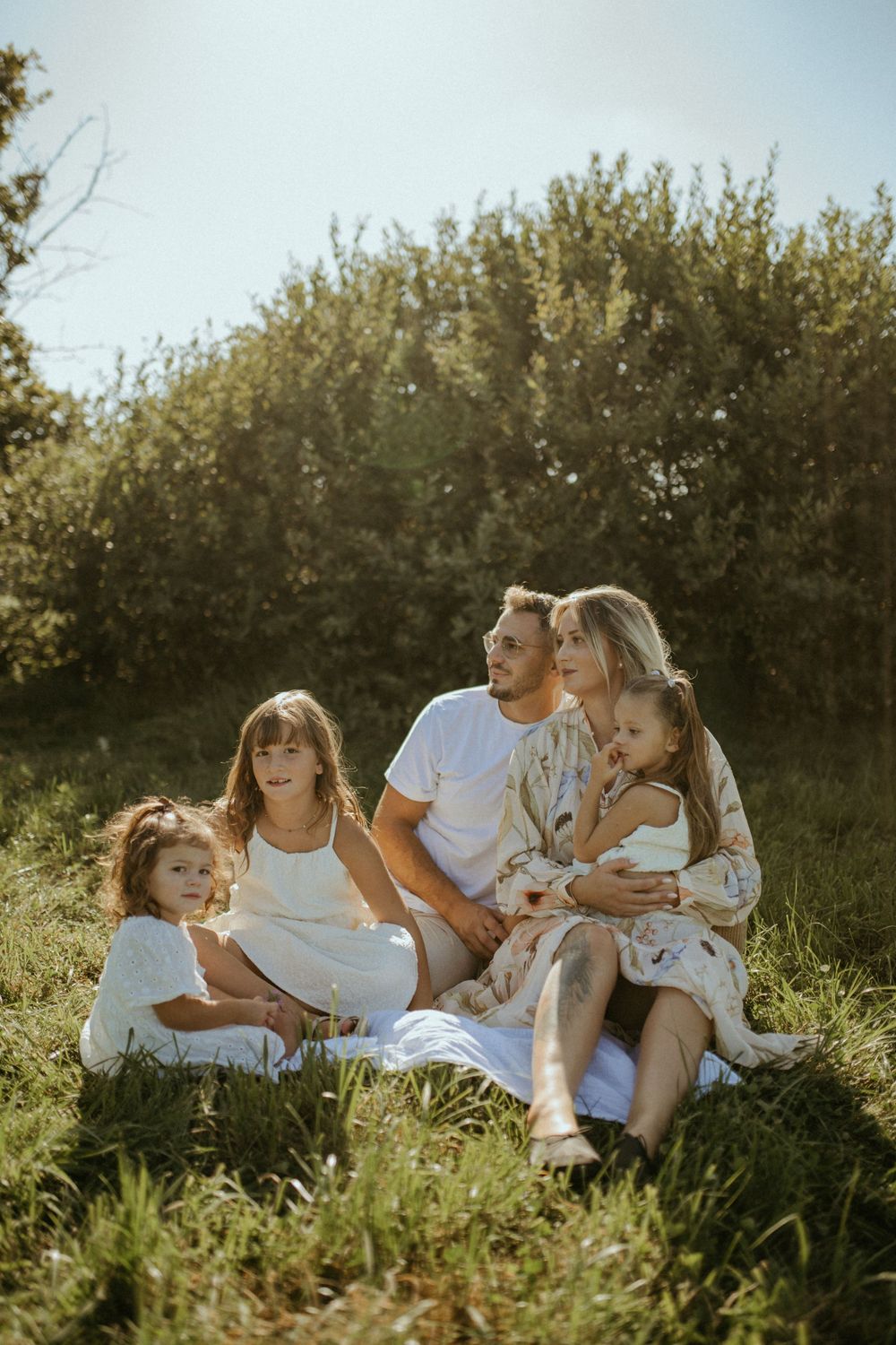 Family relaxing together on grass during golden hour with natural foliage backdrop.