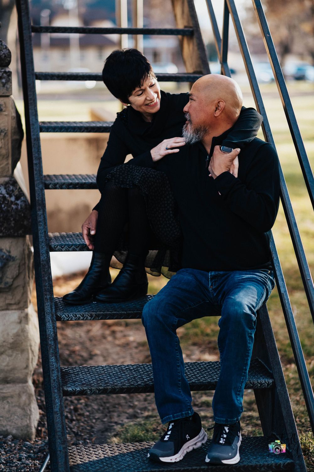Two people share an intimate moment while sitting on black metal stairs outdoors on an autumn day.