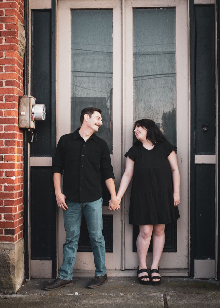 People dressed in black stand against a brick wall with glass doors in an artistic panoramic composition.