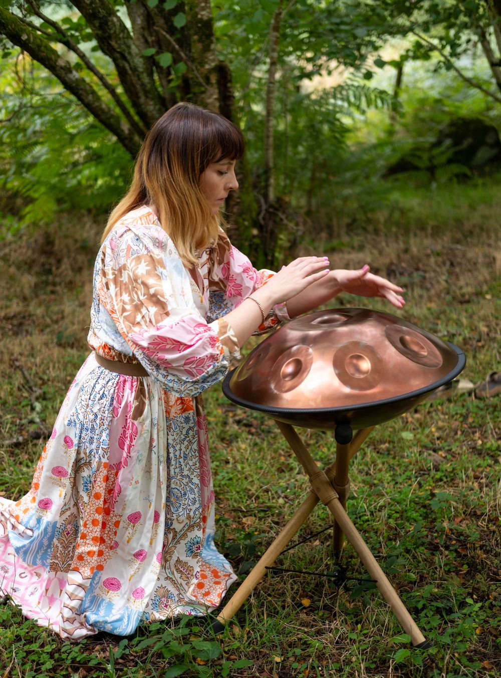 Artist in floral dress carefully crafts designs on a handmade clay pottery piece in a lush garden setting.
