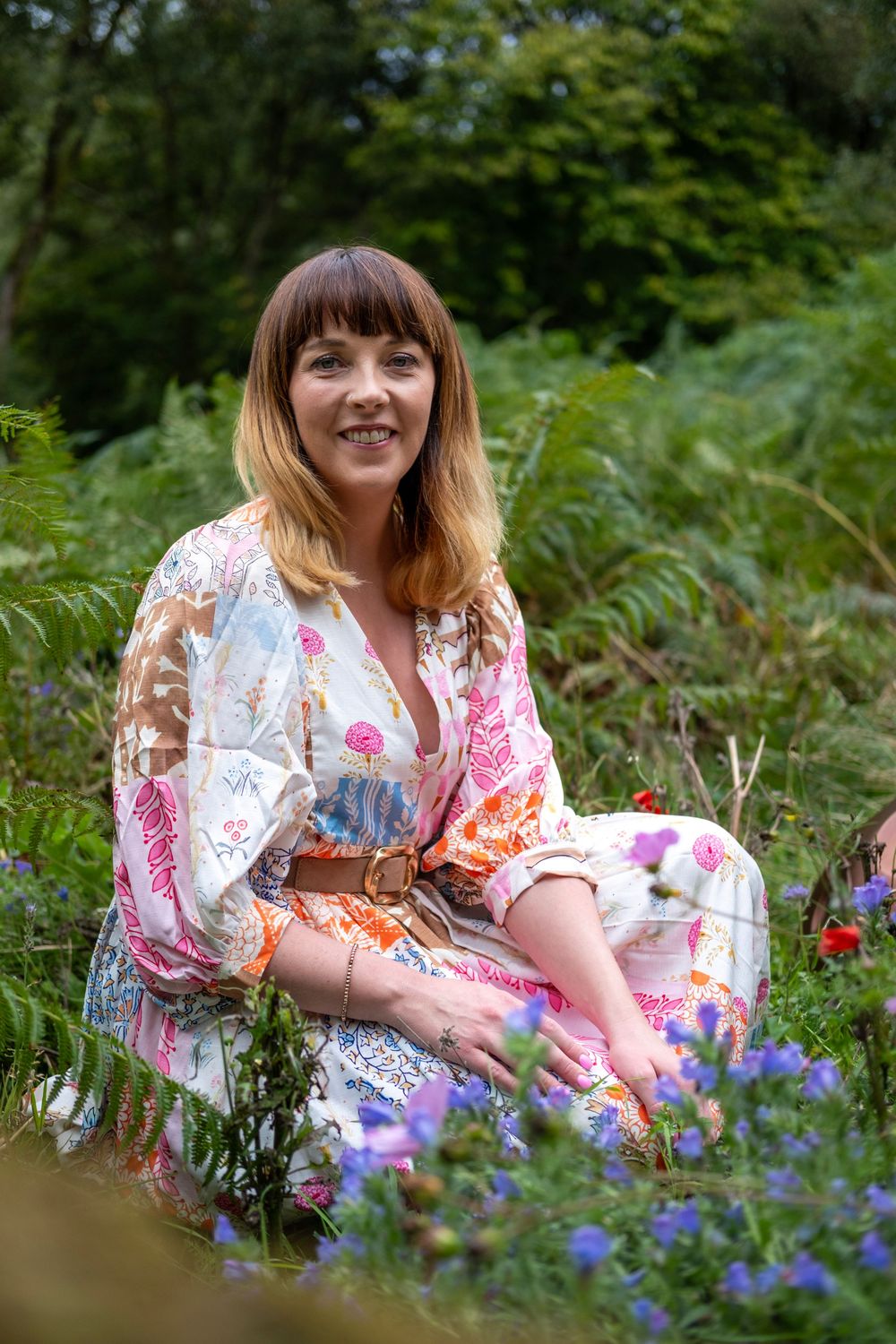 A person in a floral dress lies among colorful wildflowers in a lush garden setting.