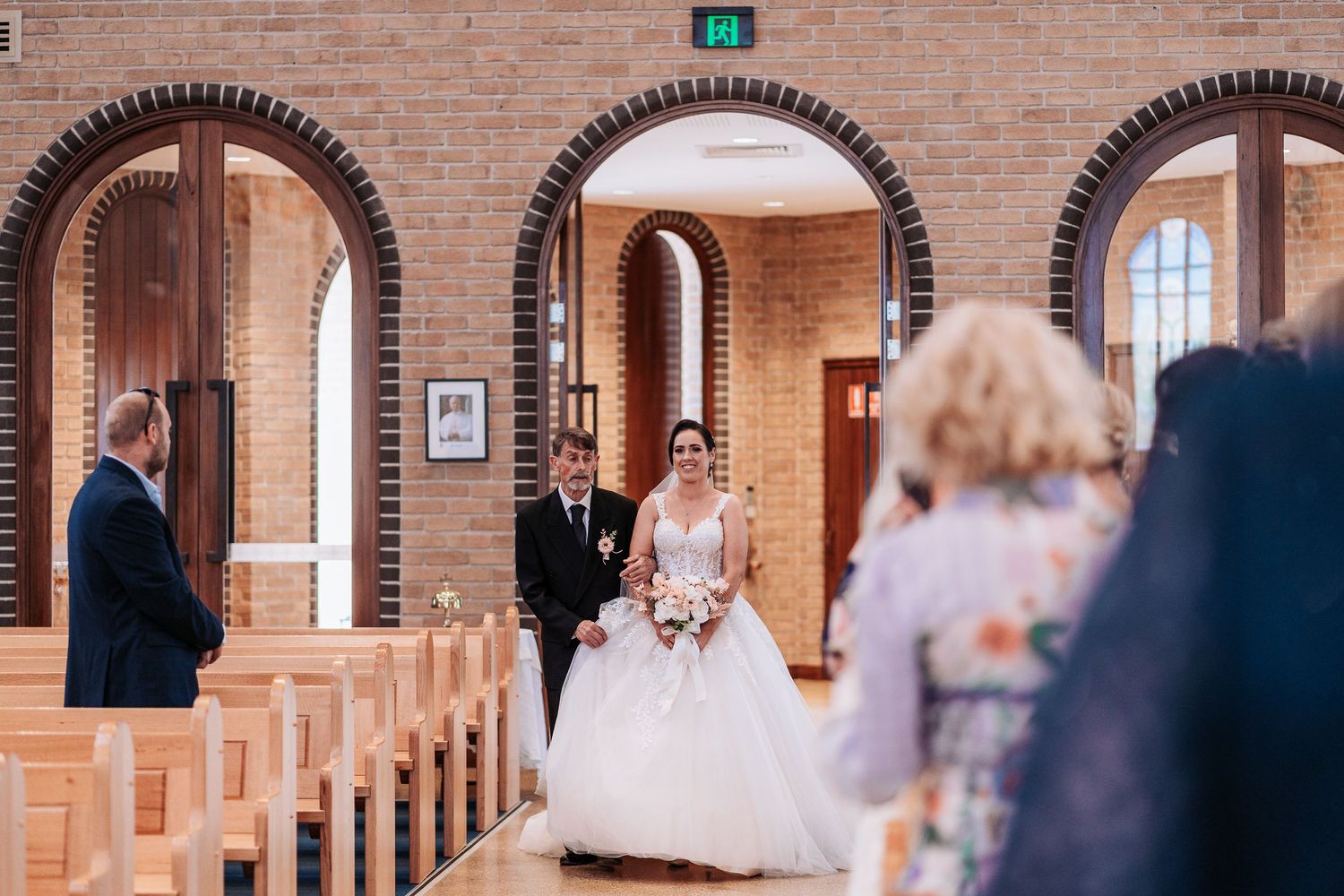 Wedding guests gather for group photos in a beautiful brick archway venue with natural lighting.