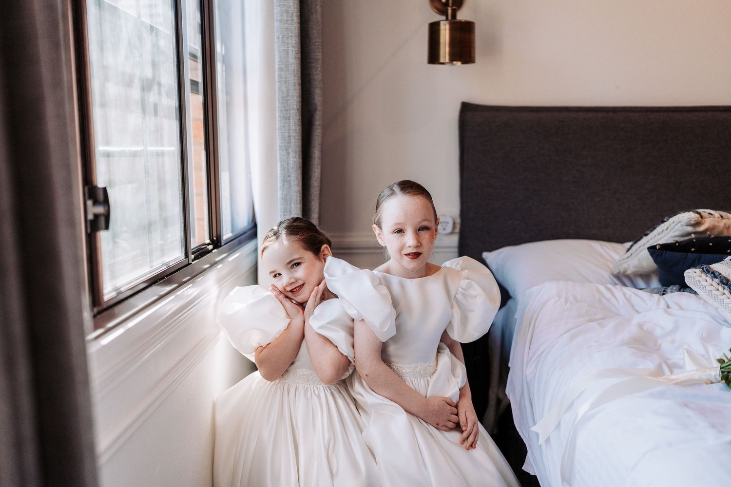 People in white and black attire gather on a bed during wedding preparations.