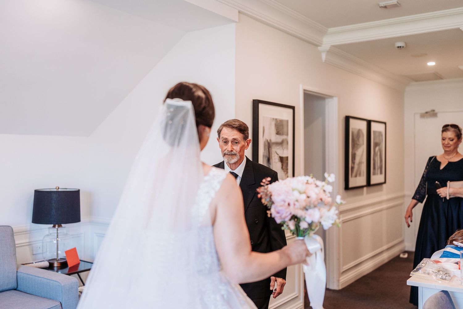 A wedding party getting ready in a bright hotel suite with floral bouquets and white decor details.