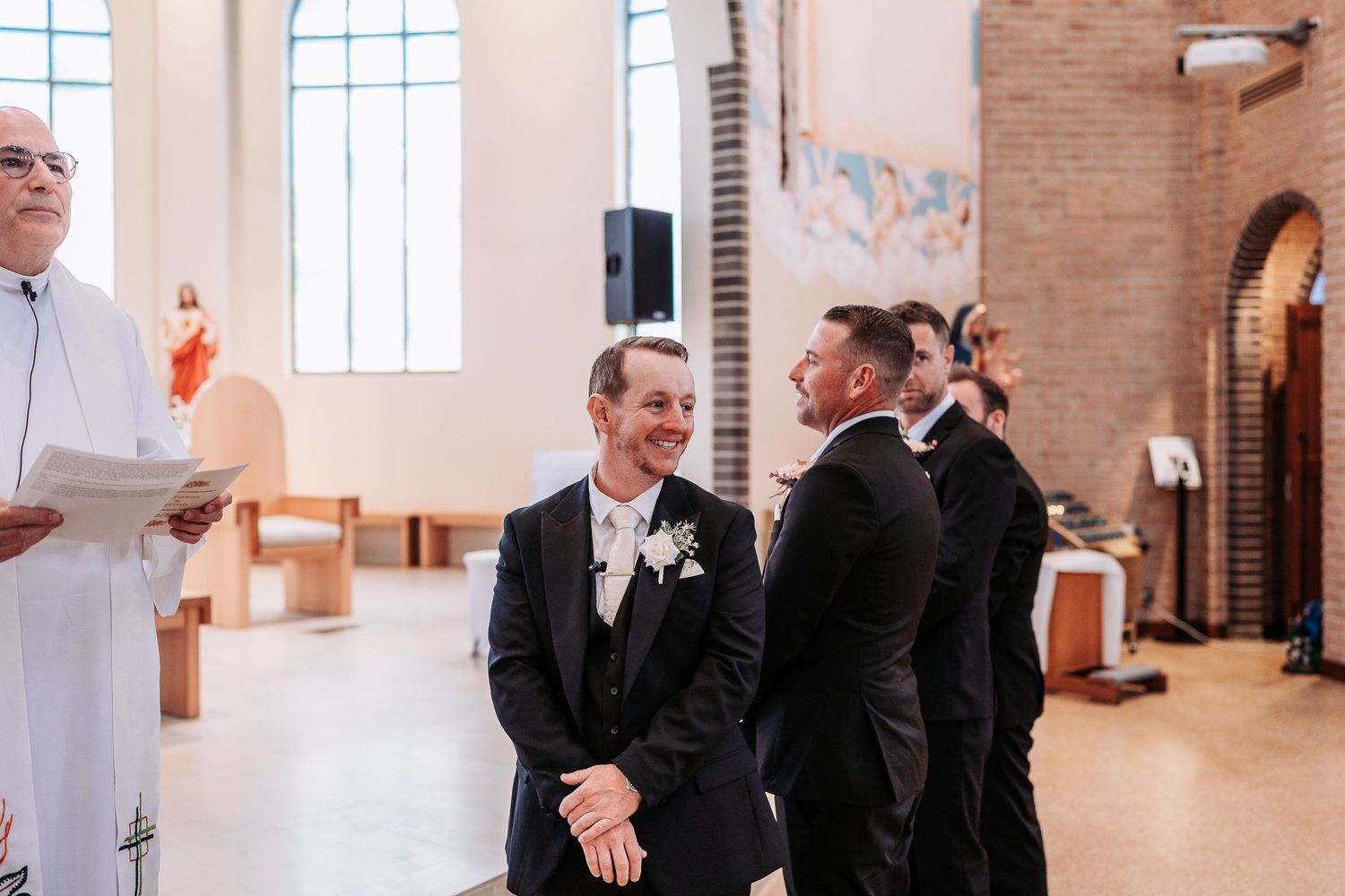 Wedding ceremony taking place in a modern church with brick walls and large windows.