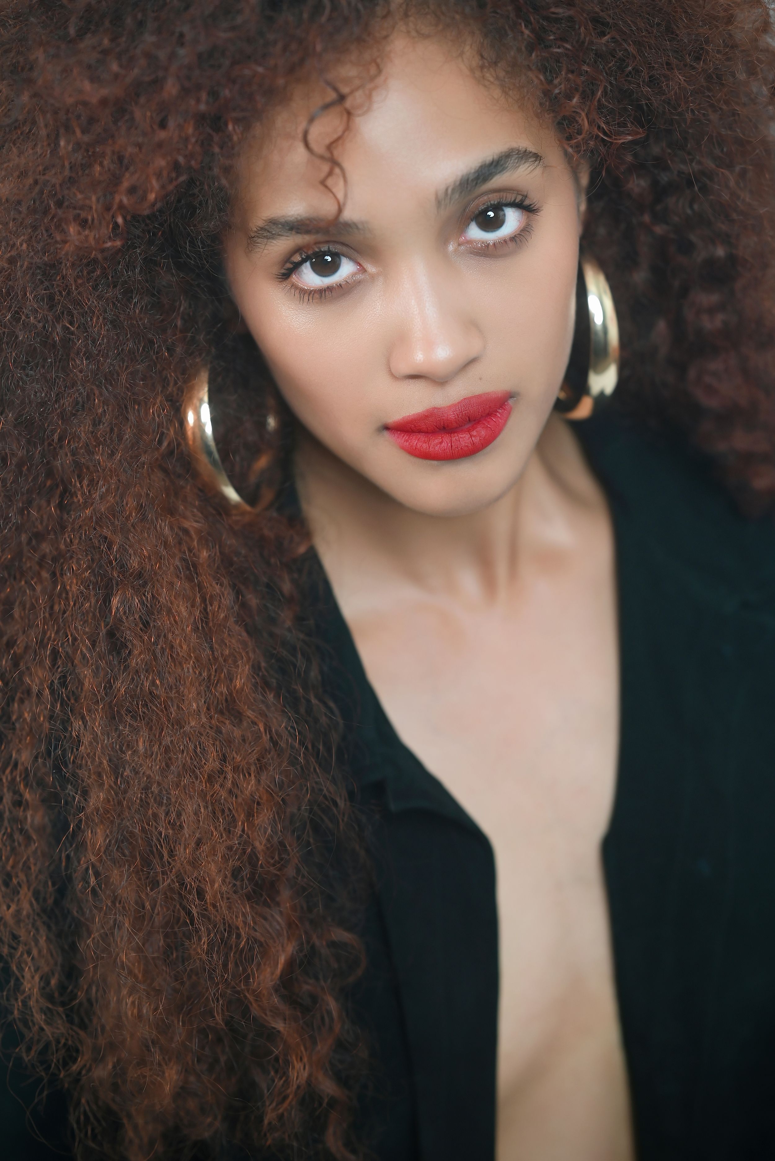 Beauty portrait with natural curly hair, red lipstick, and gold hoop earrings.