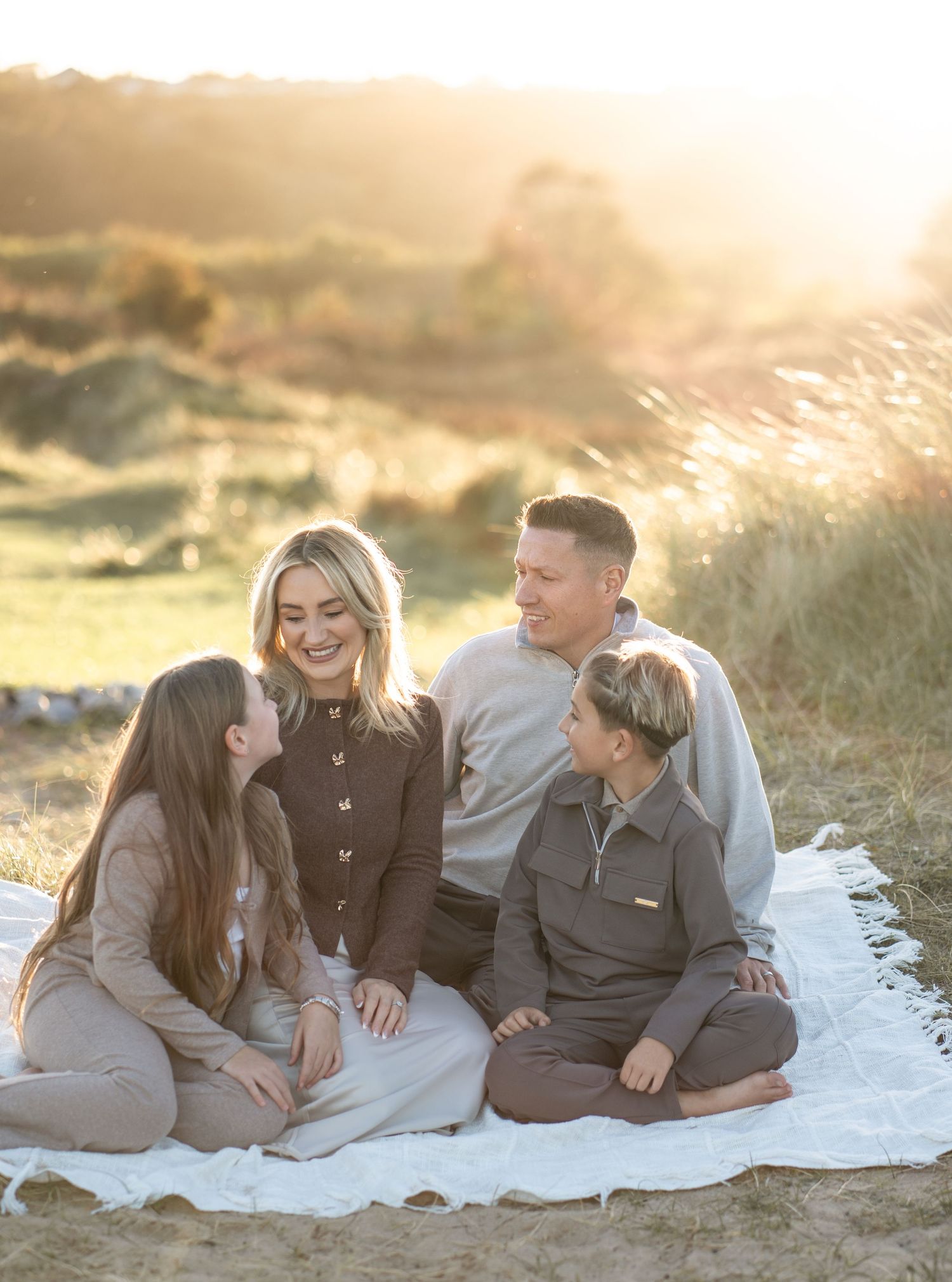 Family enjoying a tender moment together while lounging on a white blanket at sunset on the beach.