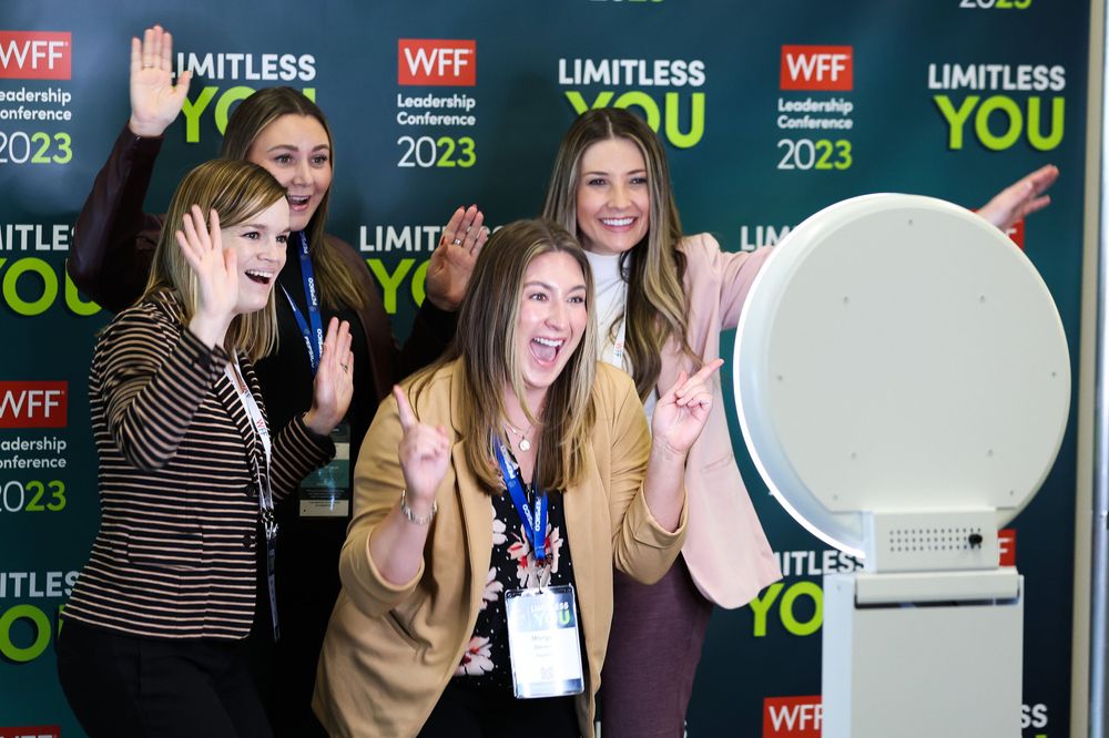 A group of women laughing together at a WFF Limitless You event in front of a branded backdrop.