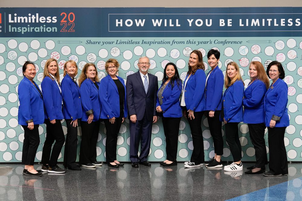 Professional group photo lineup with blue and black business attire against a branded backdrop.