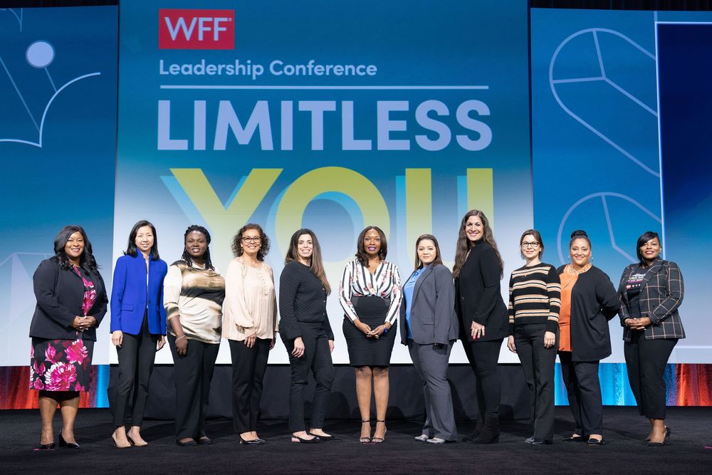 Conference attendees gather on stage at a leadership event with blue lighting and 'Limitless' signage.