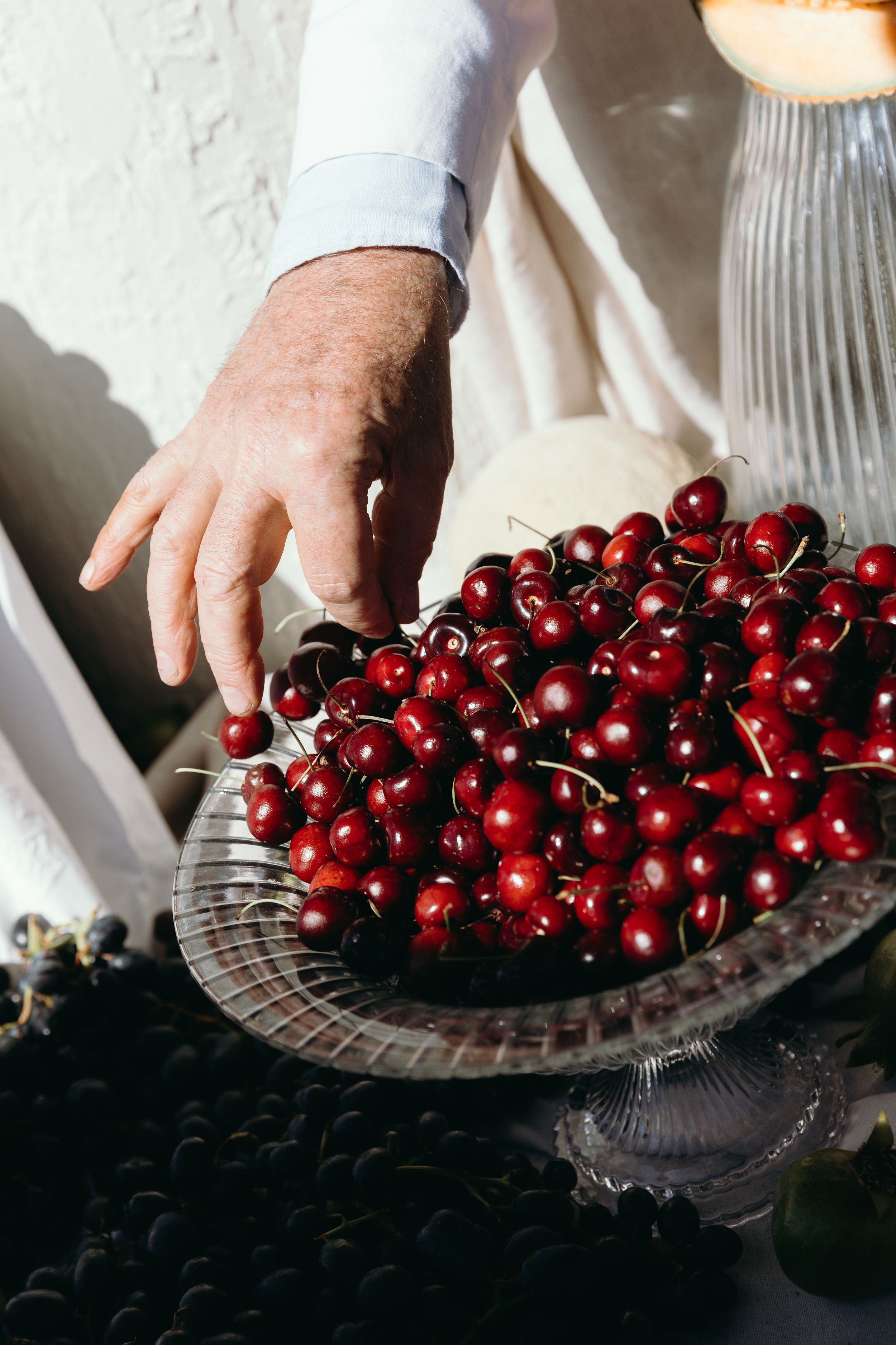 Fresh red cherries being arranged on a vintage glass serving plate in a rustic setting.