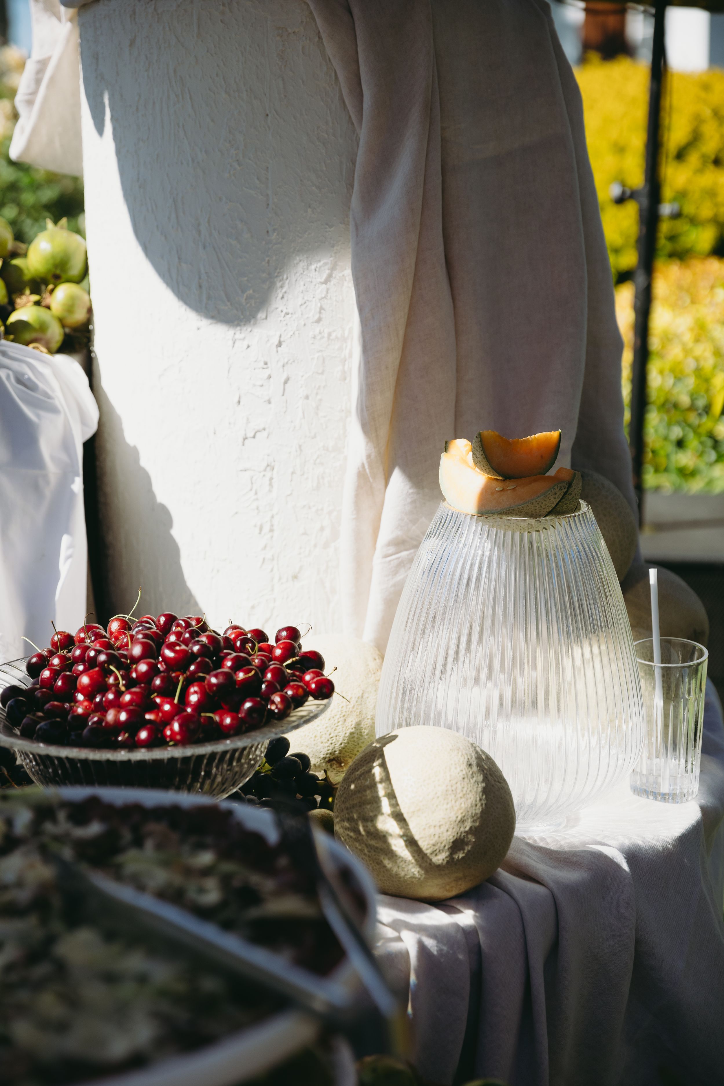 Fresh cherries and white ceramic dishes arranged on a table in natural sunlight creating a bright, minimalist still life scene.