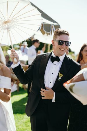 Wedding party holding white parasols outdoors on a sunny day during a summer celebration.