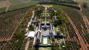 Aerial panoramic view of a large vineyard estate with rows of grape vines and buildings surrounded by green landscape.