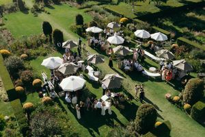 Aerial view of white party tents and umbrellas set up on a lush green lawn for an outdoor event.